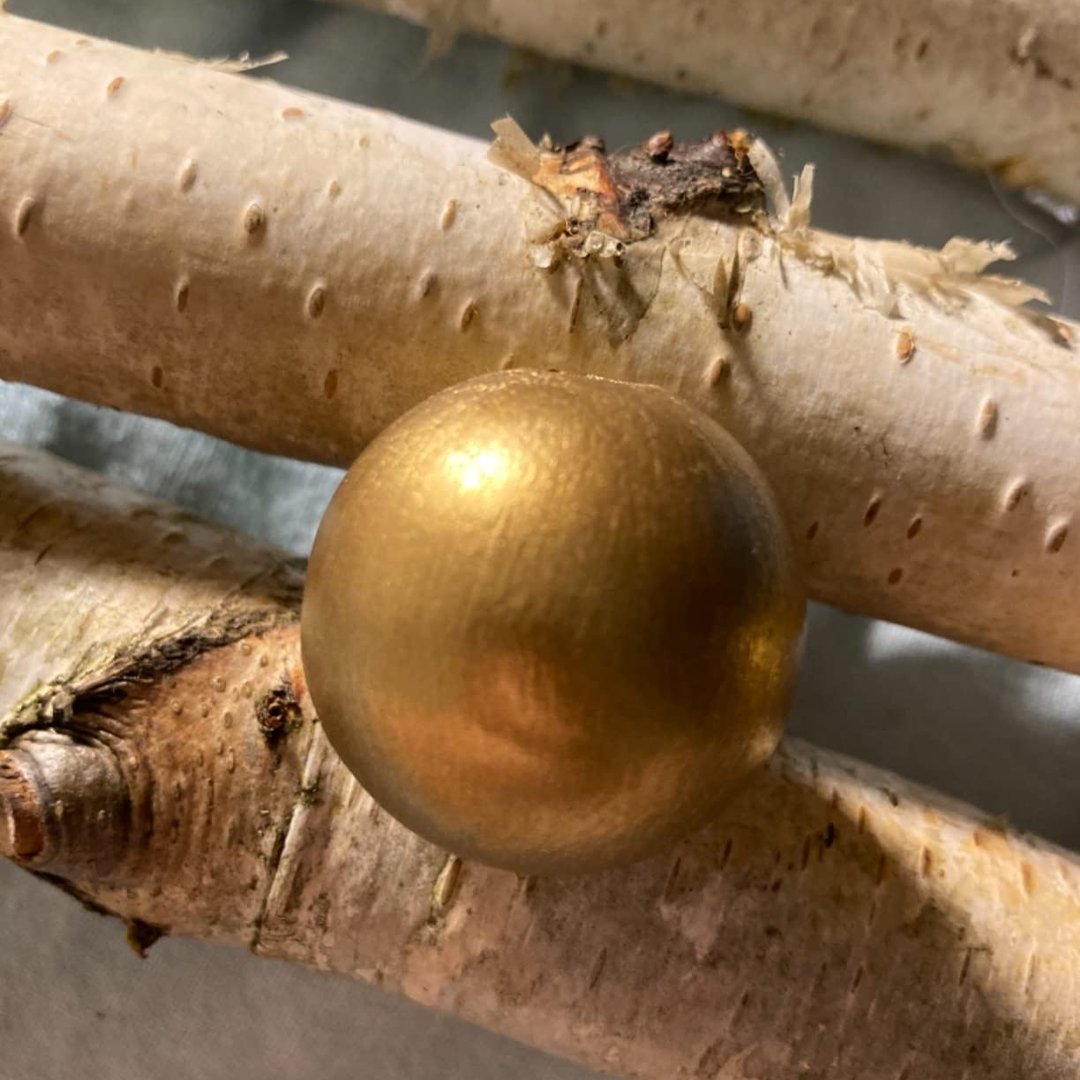 Goldfarbenes Dekoelement auf Naturholz mit warmem, metallischem Glanz.