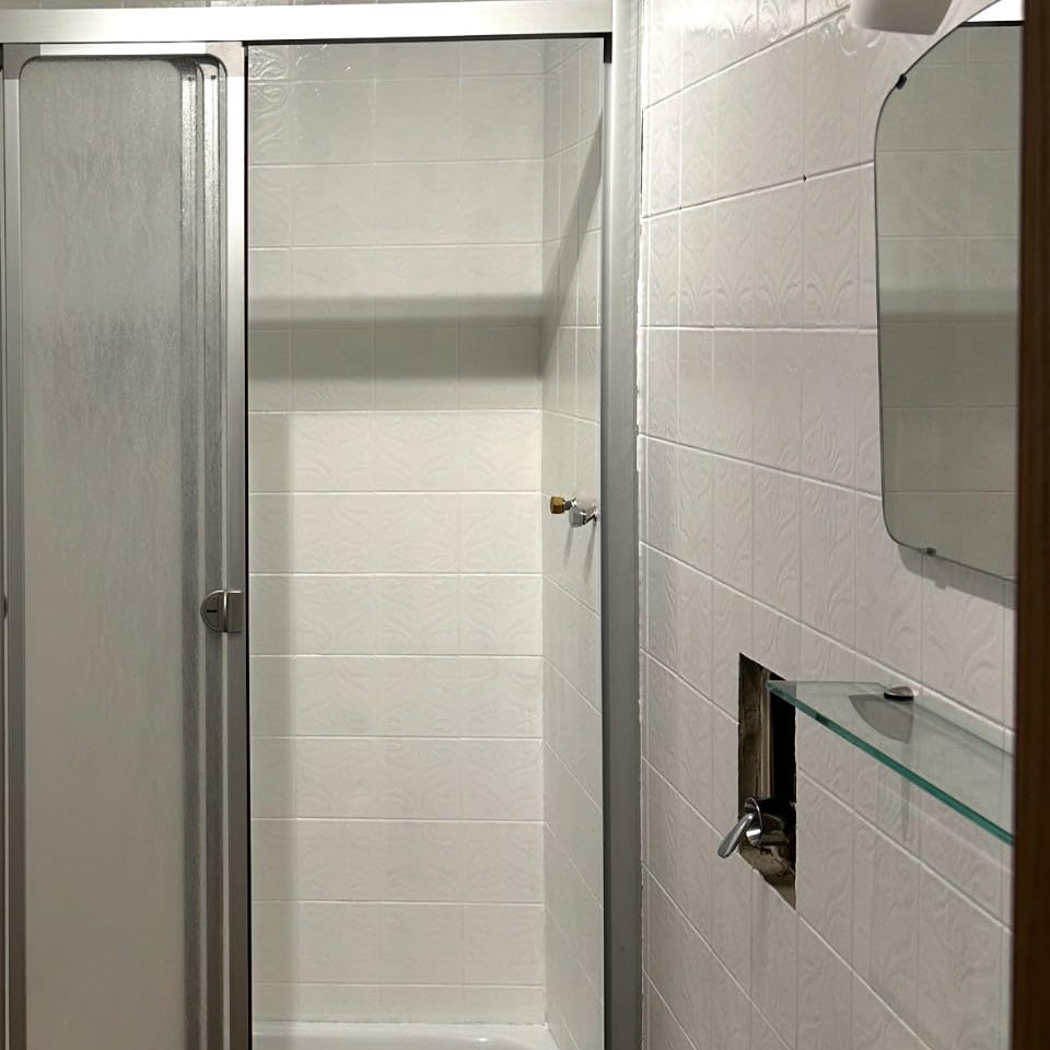 Helles Badezimmer mit Dusche und gleichmaessig weissen Wandfliesen nach der Renovierung
