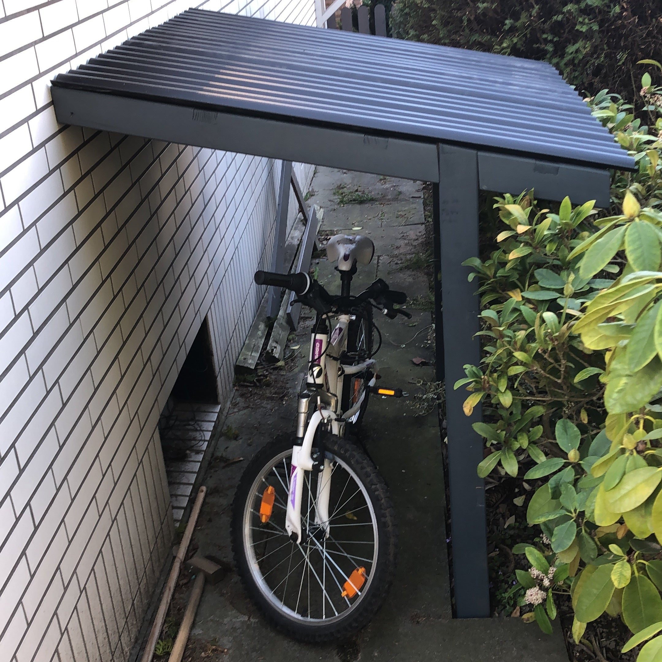 Dunkel gestrichener Fahrradunterstand aus Holz neben Hauswand als Anwendungsbeispiel fuer ColourPlus Buntlack 2in1 im Aussenbereich