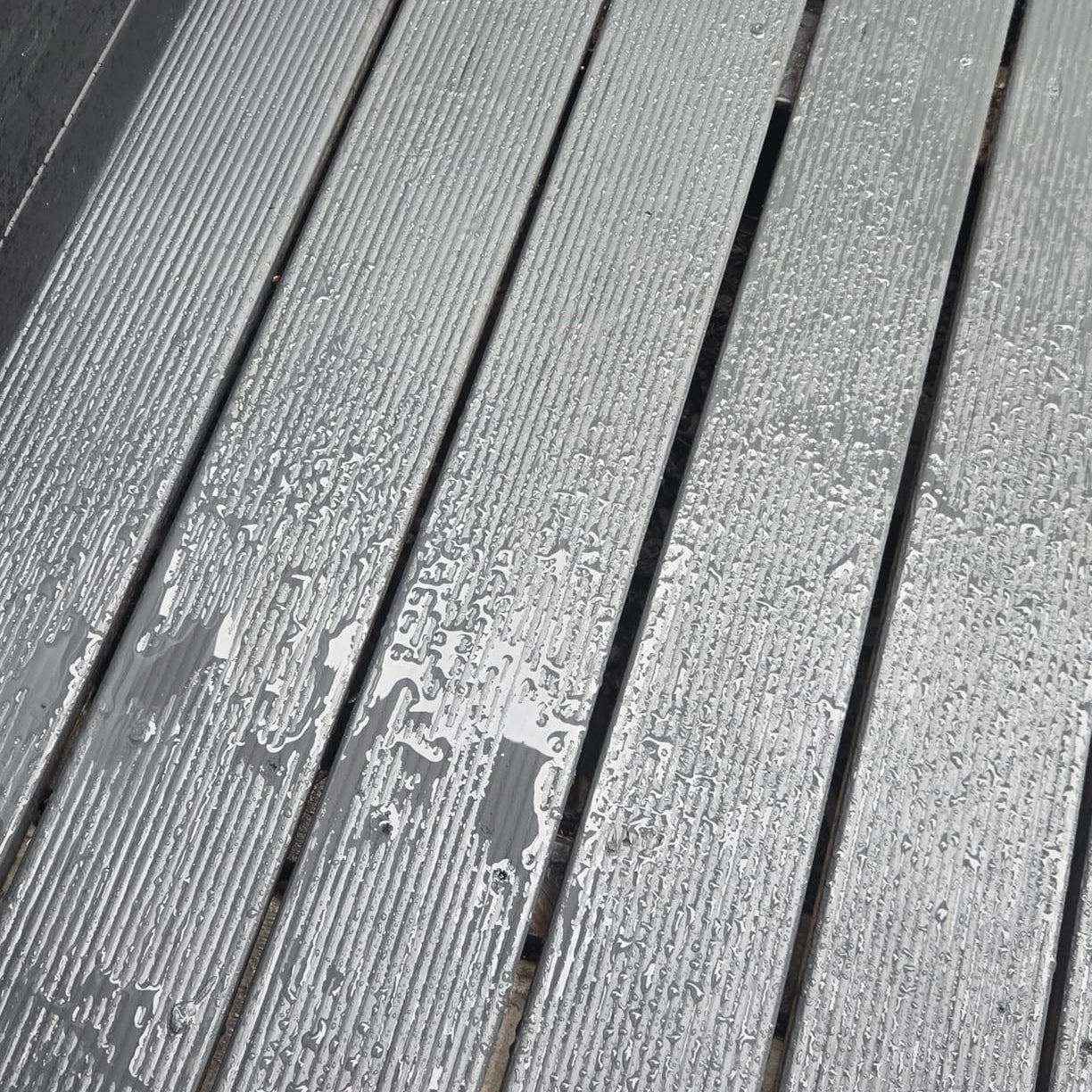 Mit ColourPlus Wetterschutzfarbe in Anthrazit gestrichene Holzbohlen mit sichtbarem Abperleffekt von Wassertropfen.