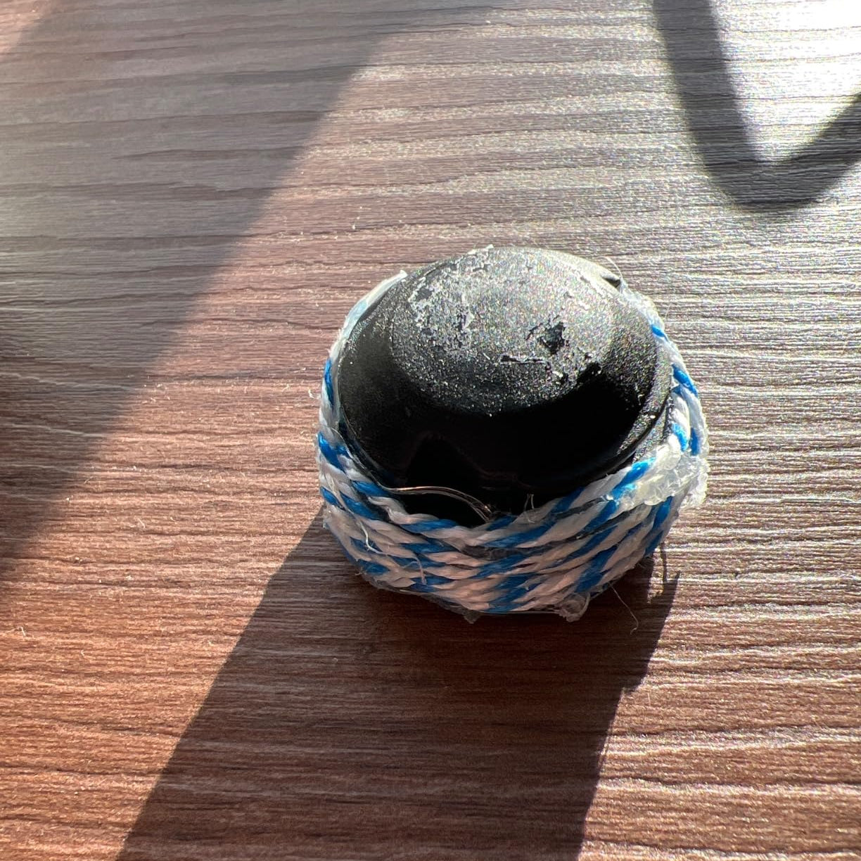 Kleines rundes Glasgefaess mit dunklem Deckel und dekorativer Kordel auf Holztisch