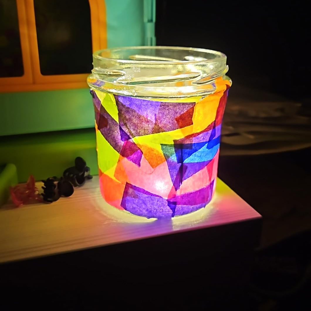 Bunt beklebtes Glaswindlicht mit transparentem Papier in leuchtenden Farben im Dunkeln