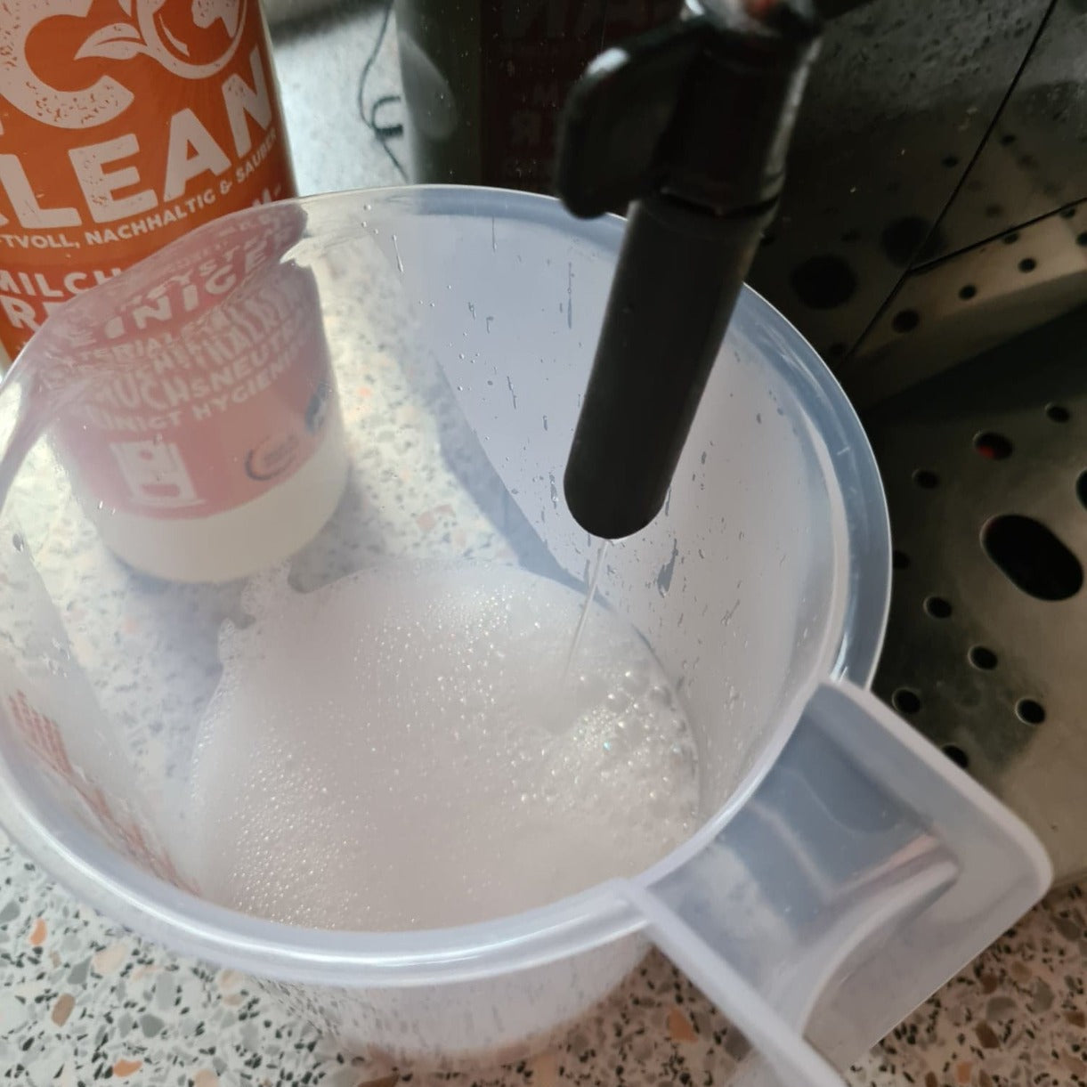 Milchaufschaeumer wird in einem Behaelter mit Reinigungslösung von Eco Clean Milchsystemreiniger durchgespuelt.