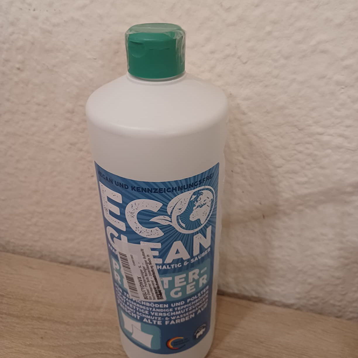 Eco Clean Polsterreiniger 1 Liter Flasche mit grünem Deckel auf Holzoberfläche vor heller Wand.