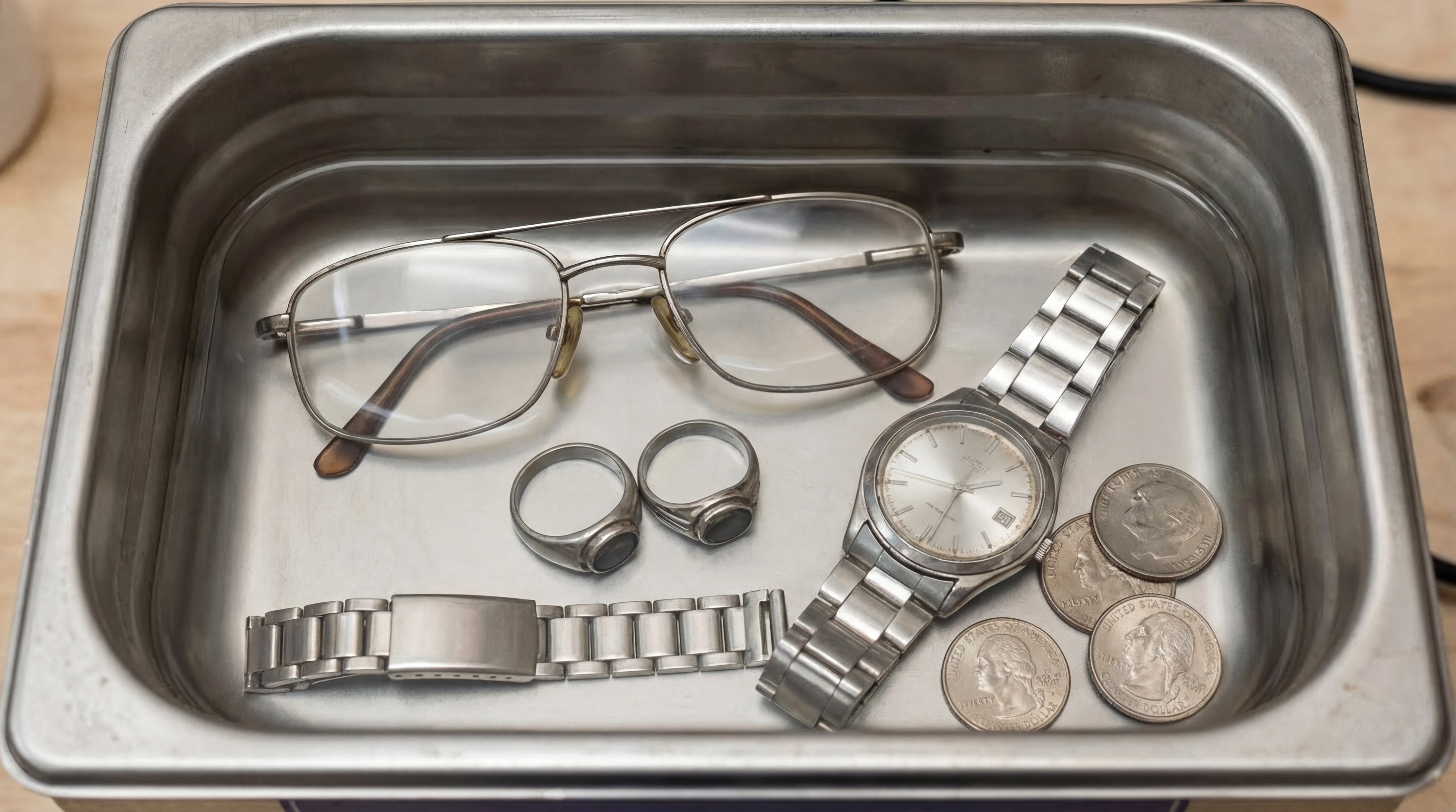 Saubere Brille, Uhr, Ringe und Muenzen in einem Metallbehaelter nach der Reinigung mit Eco Clean Ultraschallreiniger.