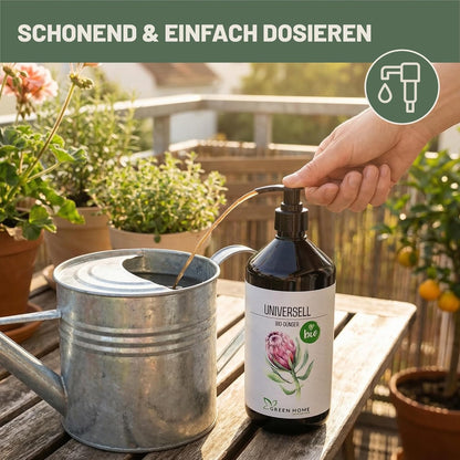 Hand dosiert Green Home Bio Dünger Universell in eine Metallgießkanne auf einem Balkon mit Pflanzen im Hintergrund