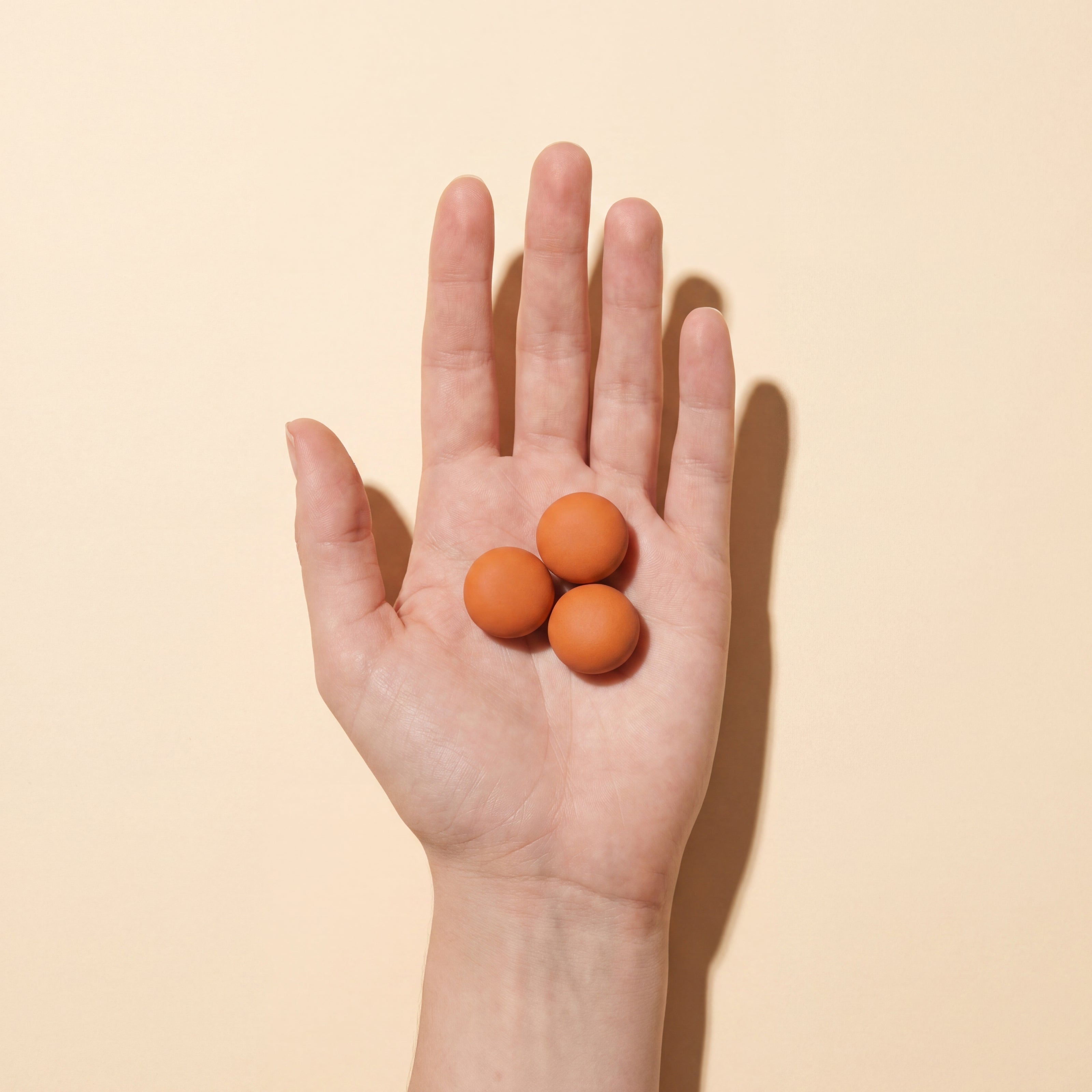 Drei warm-orange Naturobjekte in offener Hand – Symbol für pflanzliche Wirkstoffe