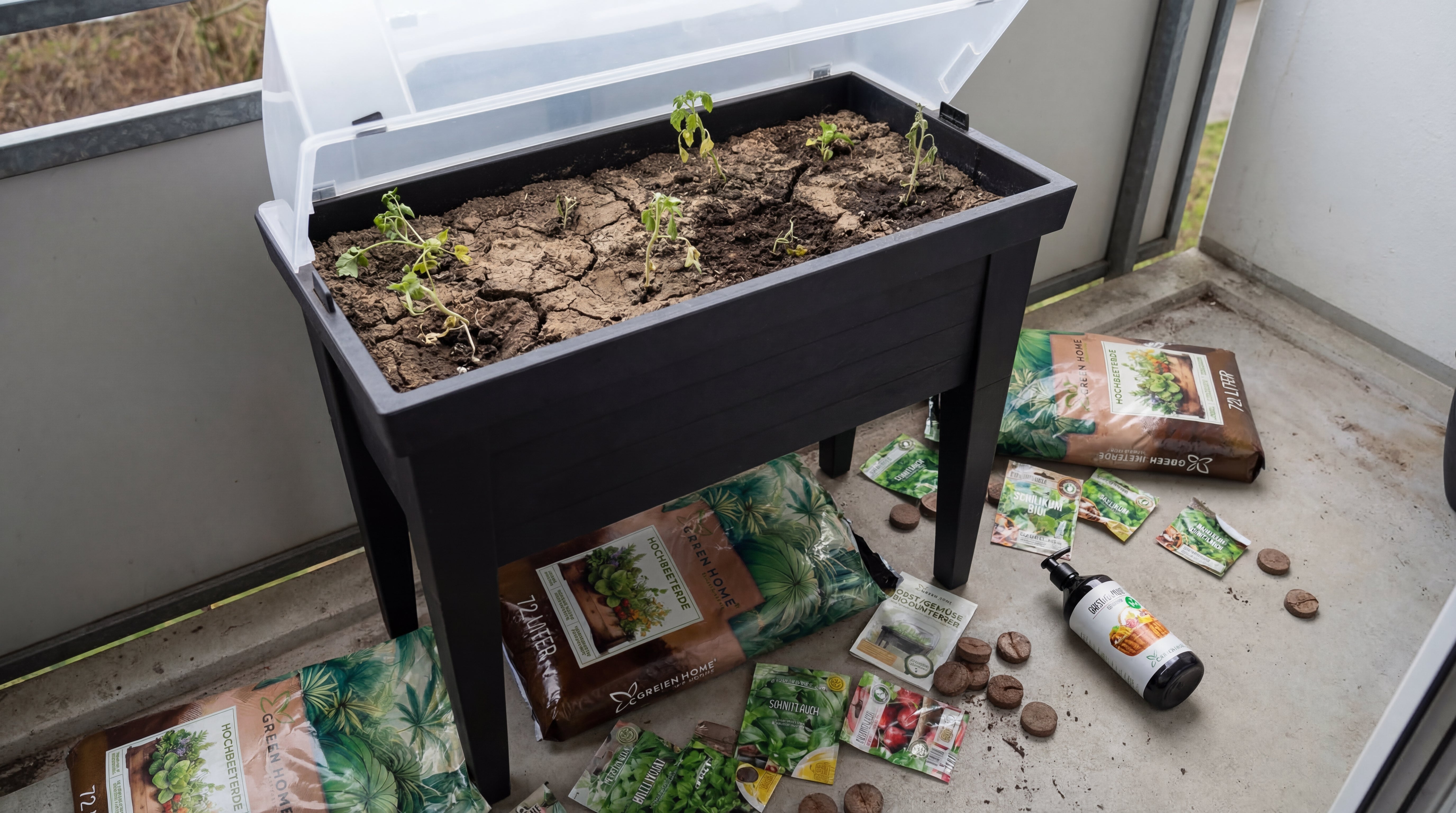 Green Home Hochbeet auf einem Balkon mit kleinen Jungpflanzen in trockener Erde, umgeben von Erdebeuteln, Samen und Zubehör.