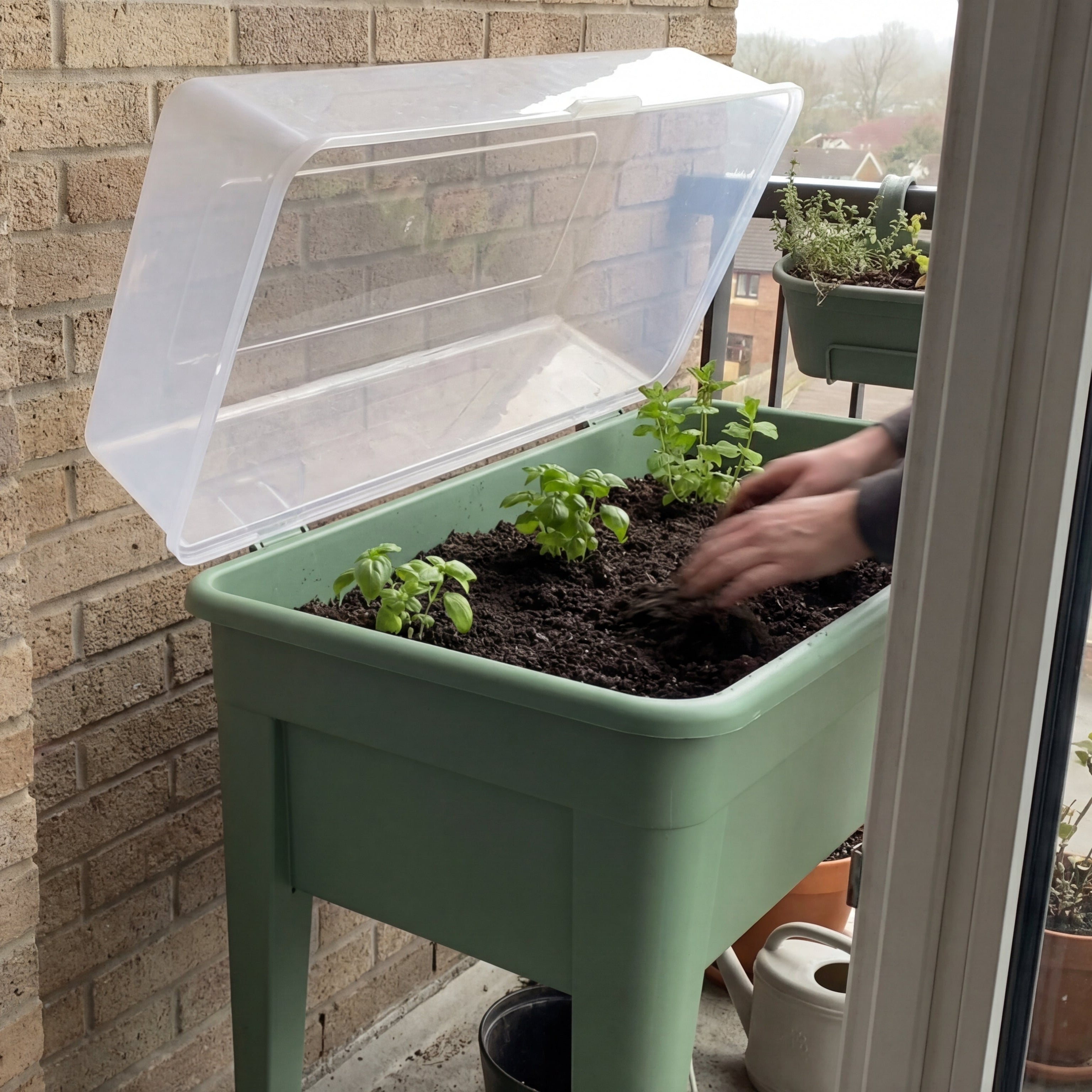 Green Home Hochbeet S mit geöffnetem Frühbeetaufsatz während des Einpflanzens von Kräutern auf einem Balkon