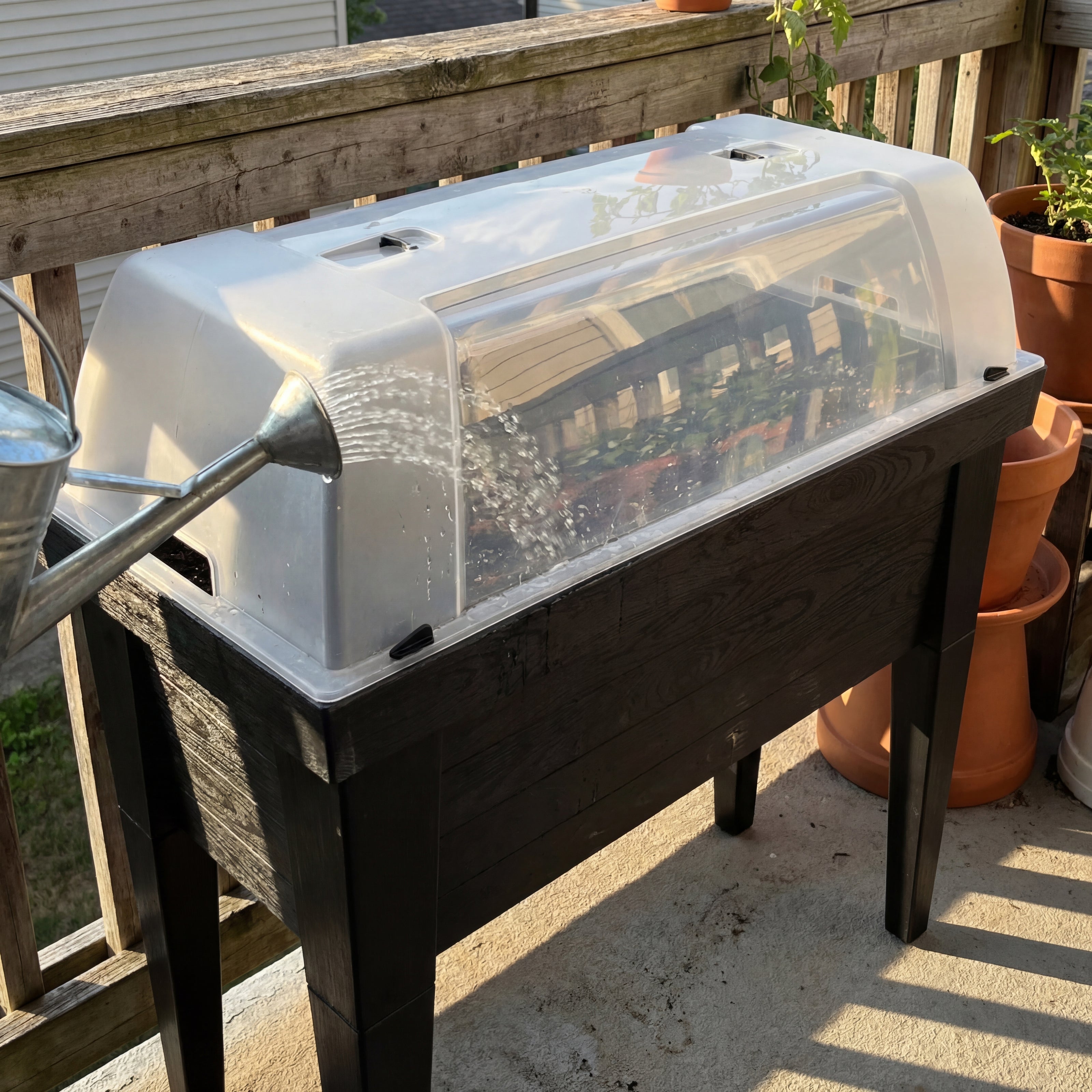 Hochbeet XL wird auf einem Balkon mit einer Giesskanne bewaessert waehrend die Haube geschlossen ist