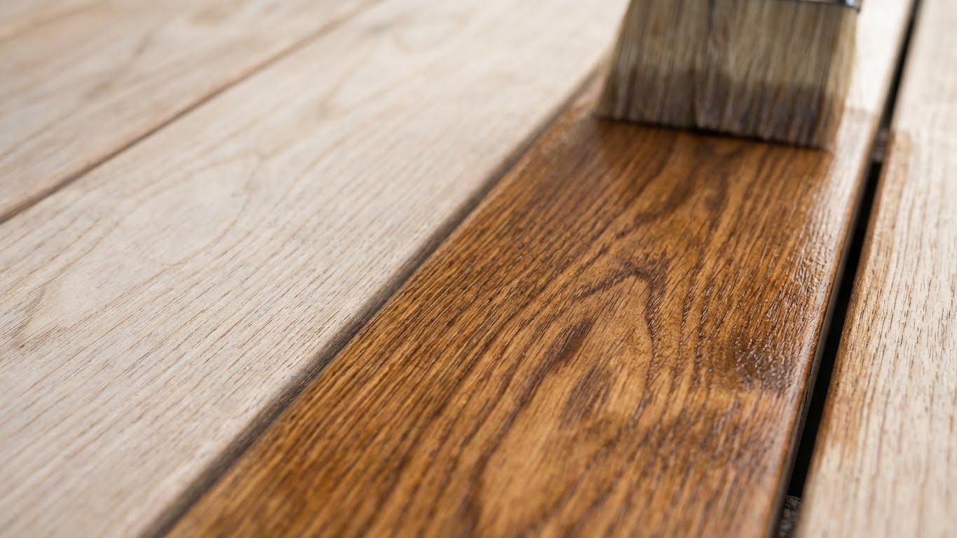 Pinsel beim Auftragen von Öl auf eine Holzbohle mit sichtbarer Betonung der Holzmaserung.