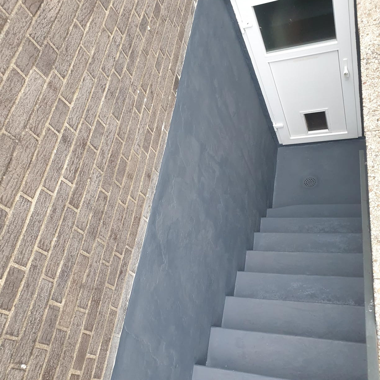 Kellertreppe mit dunkelgrau gestrichenem Sockel und angrenzender Ziegelwand