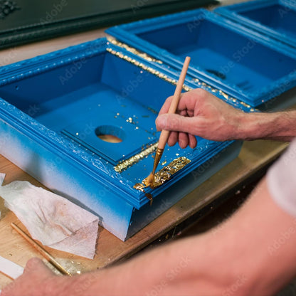Anwendung der LM Kreativ Anlegemilch beim Aufbringen von Blattgold auf einen blau lackierten Bilderrahmen