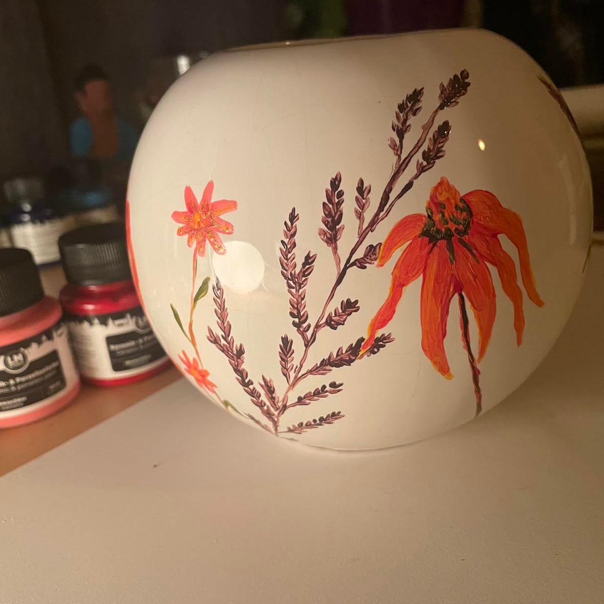 Mit LM Kreativ Keramik- und Porzellanfarbe bemalte weiße Vase mit filigranem Blumenmotiv neben Farbglaesern