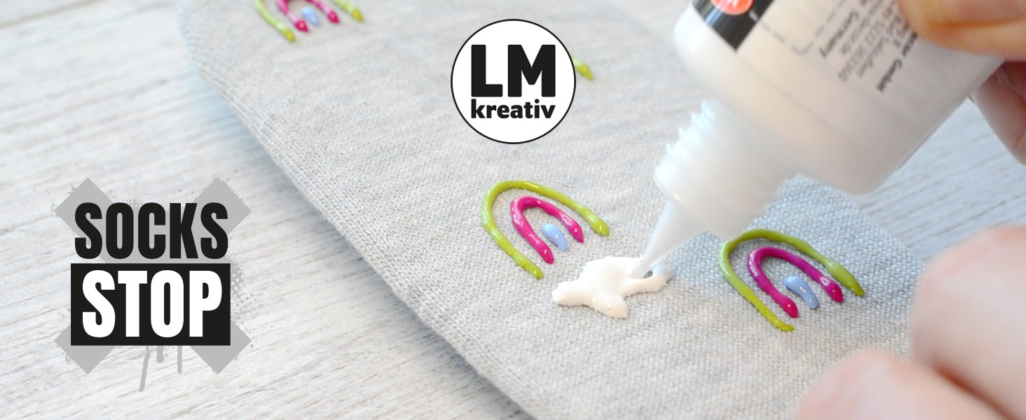 Nahaufnahme der Anwendung der LM Kreativ Socken Stopper Textilfarbe auf Stoff mit aufgetragenem weissem Stopperpunkt zwischen bunten Regenbogenmustern.