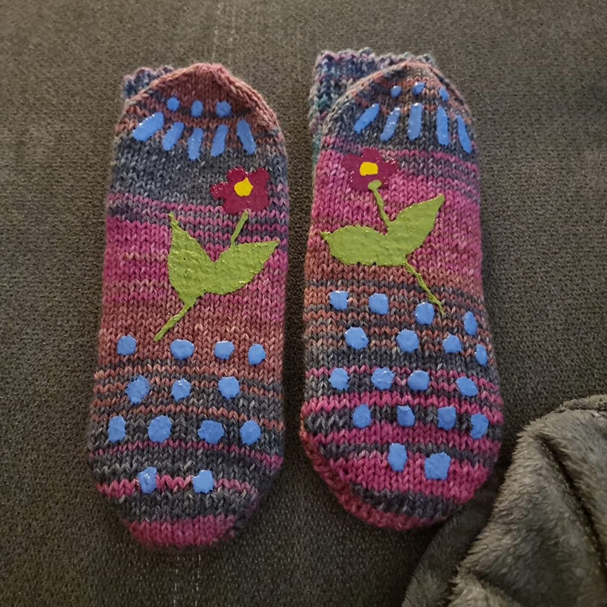 Gestrickte Socken mit buntem Blumenmuster und blauen rutschfesten Stopperpunkten auf der Unterseite, gestaltet mit LM Kreativ Socken Stopper Textilfarbe.