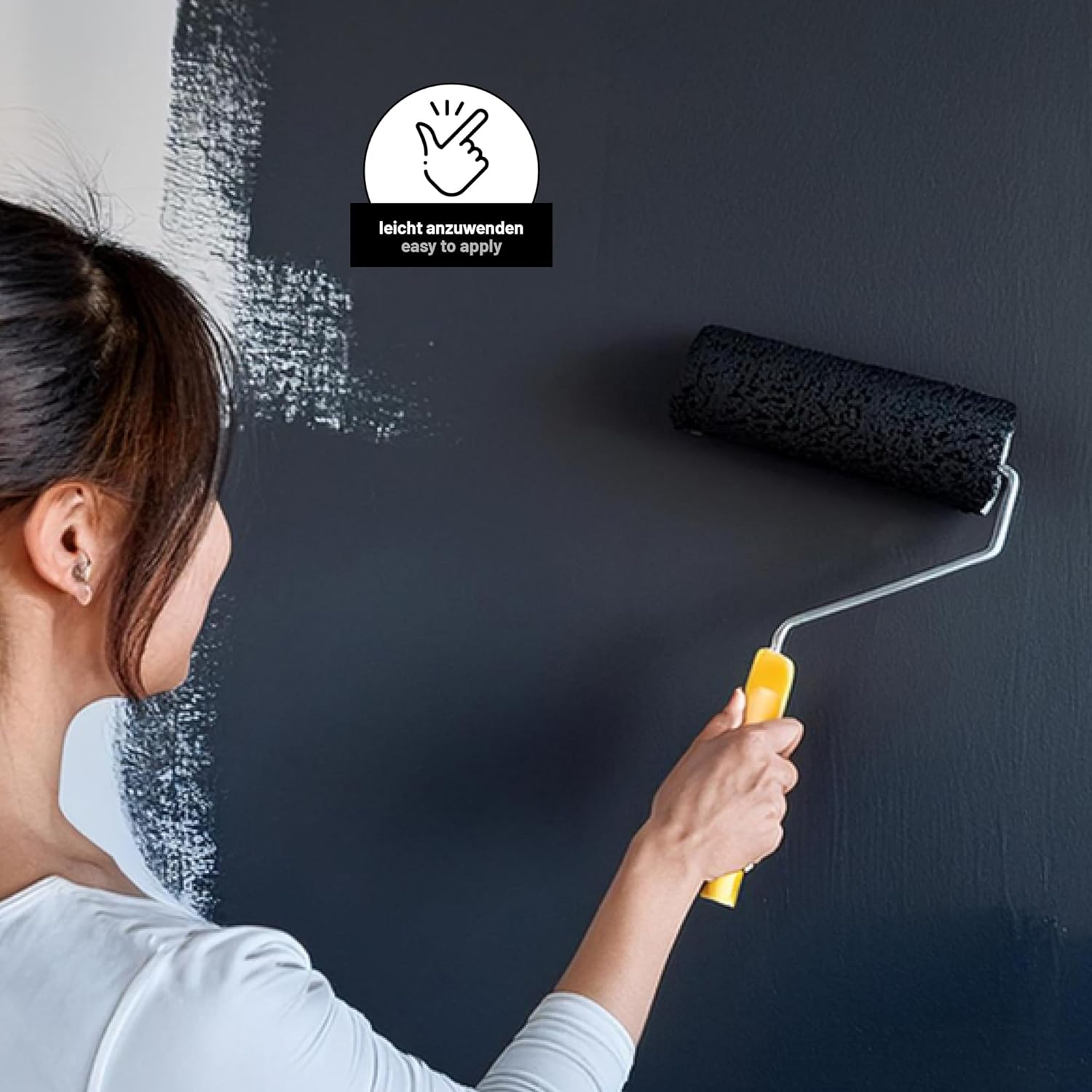 Person traegt schwarze Tafelfarbe mit einer Farbrolle gleichmaessig auf eine Wand auf