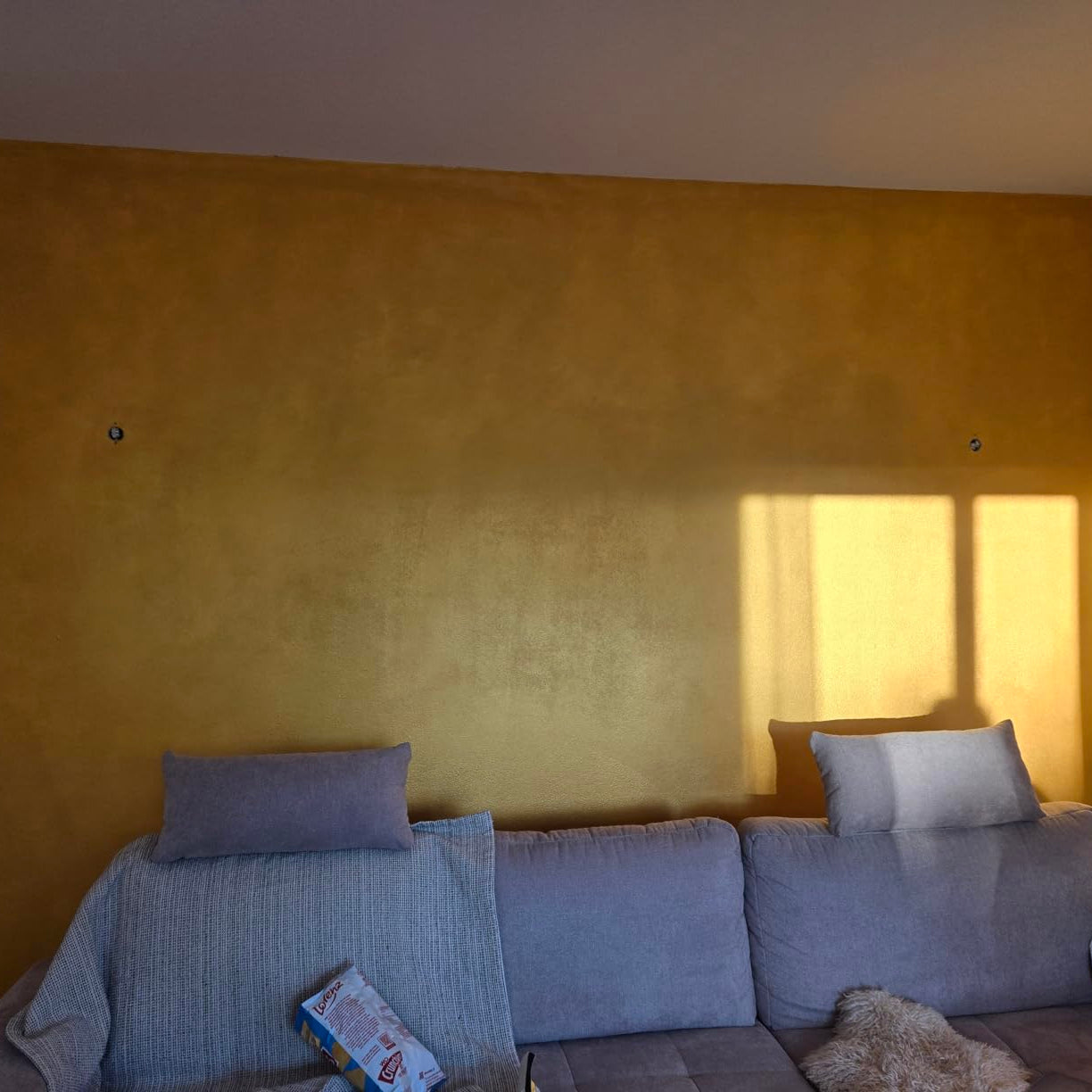 Wohnzimmerwand in Gelb-Gold Metallic Wandfarbe mit warmem Lichtspiel und seidigem Glanz.