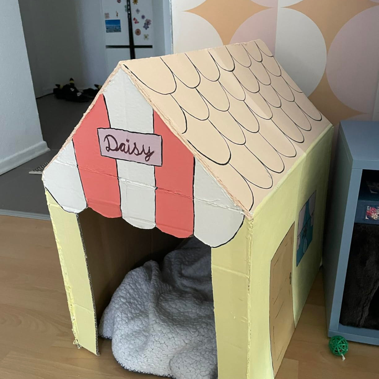 Selbstgestaltetes Papphaus in Pastellfarben bemalt mit Markise und Namensschild als kreatives DIY Projekt.
