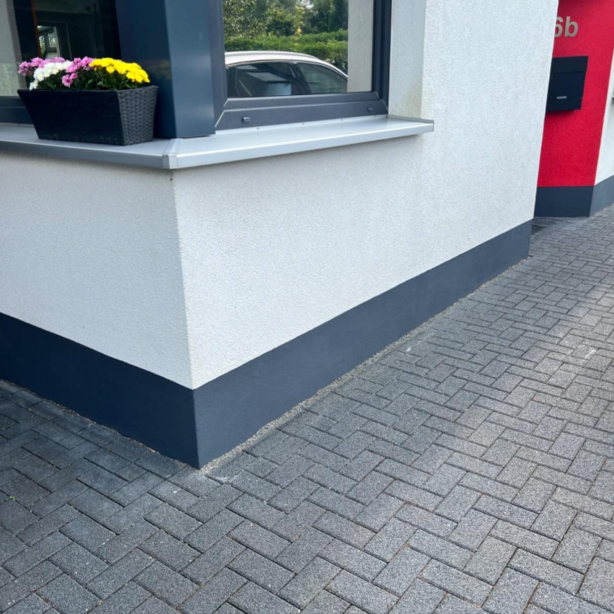 Grau gestrichener Sockelbereich einer Hausfassade mit Fensterbank und Pflastersteinen im Vordergrund