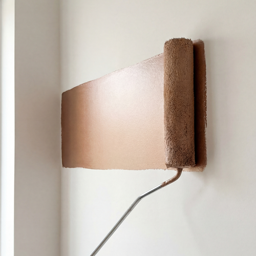 Ein Farbroller trägt beige Wandfarbe in einem gleichmäßigen Streifen auf eine helle Innenwand auf.