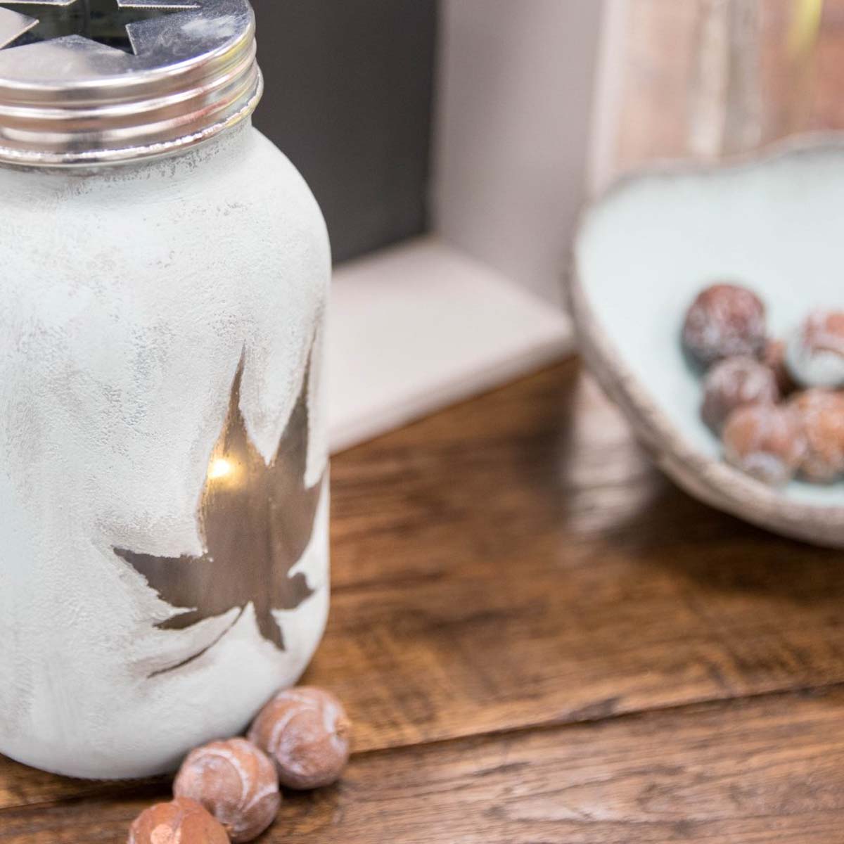 Detailaufnahme eines Windlichts aus Glas mit Ahornblatt Motiv und Kerzenschein als herbstliche Dekoration.