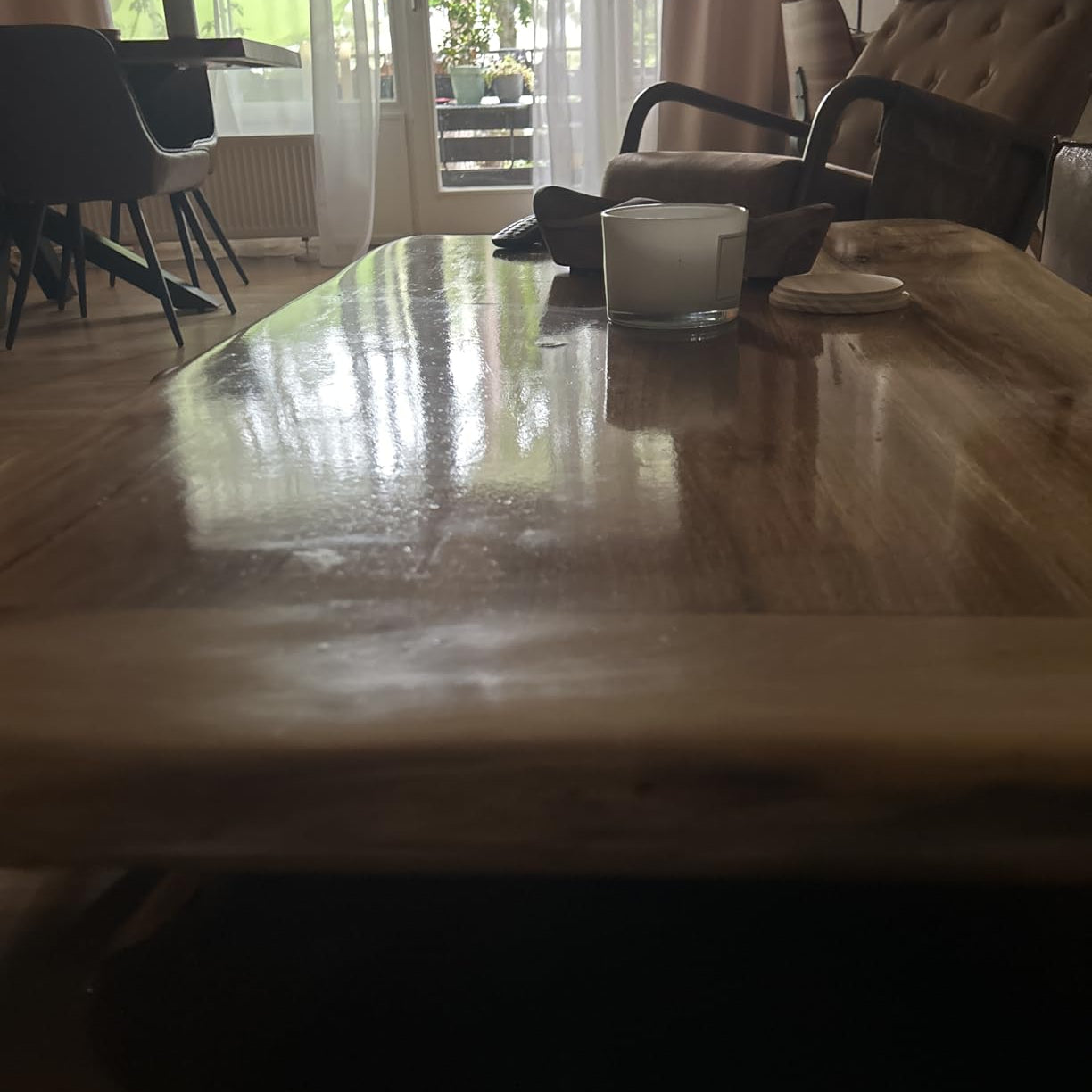 Wohnzimmer mit hochglaenzendem Holztisch, Kerze und Sesseln im Hintergrund bei Tageslicht